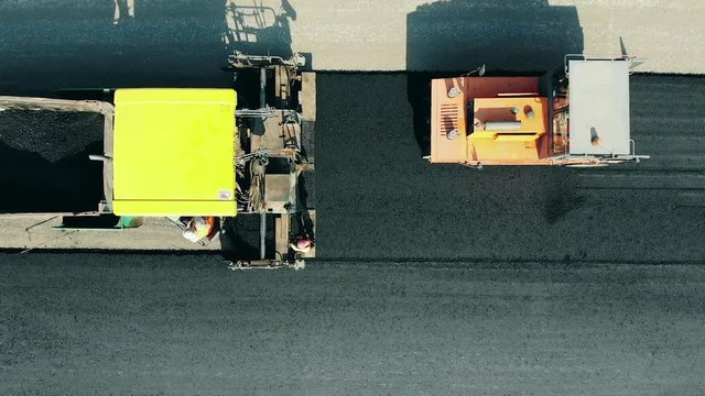 Road rollers are spreading bitum in a top view. Asphalt paver machine on a road construction site.