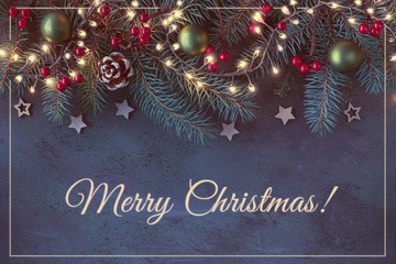 Christmas background with fir twigs, red berries, cones and Xmas lights on dark abstract background with golden greeting text "Merry Christmas" and shiny frame.