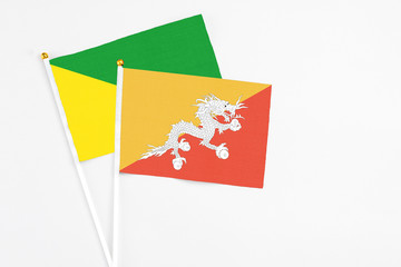 Bhutan and French Guiana stick flags on white background. High quality fabric, miniature national flag. Peaceful global concept.White floor for copy space.