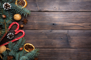 Frame of Christmas tree cones oranges caramel cane nuts on dark wooden background. Copy space. Flat lay.