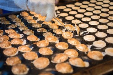 Tiny Dutch pancakes being cooked on a pancake griddle and being turned by a cook small miniature...