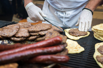 Midsection of a male cook grilling traditional Balkan food flatbread sausages patties on a grill at a food festival depth of field