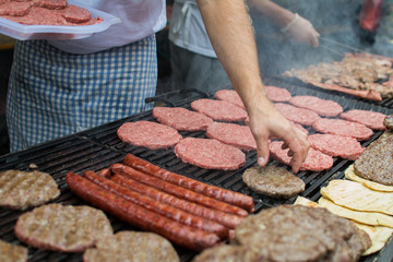 Midsection of a male cook grilling traditional Balkan food flatbread sausages patties on a grill at a food festival depth of field
