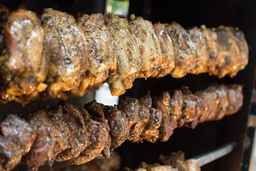 Chickens on a skewer rotating in an oven baking at a food festival, covered in herbs