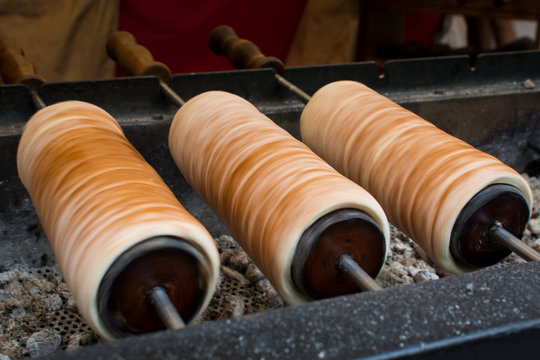 Traditional Hungarian chimney cake, trdelnik, Kürtőskalács, being baked over charcoal grill on a food stand, spinning and rotating until cooked