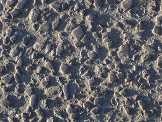 Weathered asphalt with exposed gravel sunlit from left