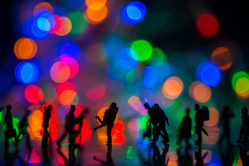 Fototapeta na wymiar Miniature toy - Silhouette of a couple hugging together among busy commuters crowd with colorful bokeh lights, happiness concept.