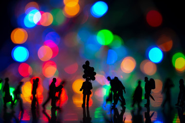 Fototapeta na wymiar Miniature toy - Silhouette of a man holds colorful balloons among busy commuters crowd with colorful bokeh lights, waiting for someone concept.