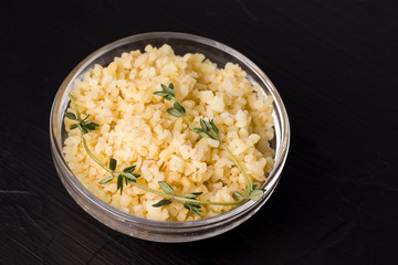 ready-made bulgur porridge with greens on a black background in a transparent bowl