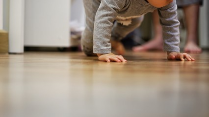 toddler crawling on clean bedroom wooden floor while mother watching in the back. child development and baby growing up.