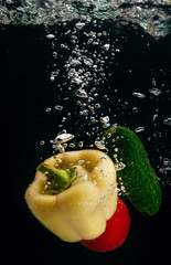 Naklejka na ściany i meble Yellow pepper, green cucumber and red tomato drop in water on a black background.
