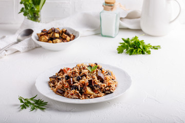 Eggplant pilaf served in white plate. Rice with aubergine,  black raisins and tomatoes on white table. Healthy vegetarian food concept.