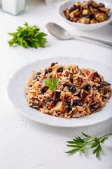 Eggplant pilaf served in white plate. Rice with aubergine,  black raisins and tomatoes on white table. Healthy vegetarian food concept.