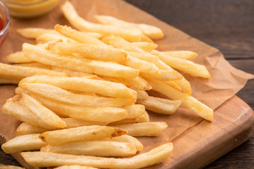 Golden yummy deep French fries on kraft baking sheet paper and serving tray to eat with ketchup and yellow mustard, top view, lifestyle.
