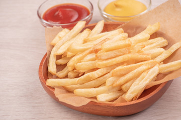 Golden yummy deep French fries on kraft baking sheet paper and serving tray to eat with ketchup and yellow mustard, top view, lifestyle.