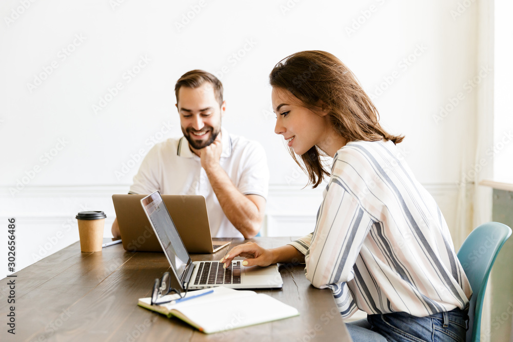 Wall mural Pleased couple colleagues work with laptops