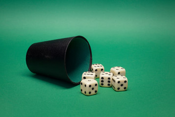 A black playing cup with several dices in the foreground