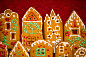 Christmas background. Red table cloth with town of cute gingerbread houses decorated with icing, Christmas lights, glitter and fir tree branches. Holiday mood. 