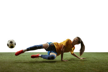 Young female soccer or football player with long hair in sportwear and boots kicking ball for the goal in jump on white background. Concept of healthy lifestyle, professional sport, motion, movement.