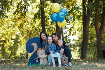 Family life. Portrait of parents and their children in the Park. Birthday of a two year old boy. Decor with the number two with lion and balloons.