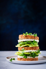 Avocado, cucumber and feta cheese sandwich decorated with micro-greens and multi-grain bread on a simple wooden stand for a healthy breakfast. Selective focus.