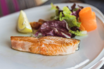 Salmon grilled on the white plate, serve with vegetables and lemon.