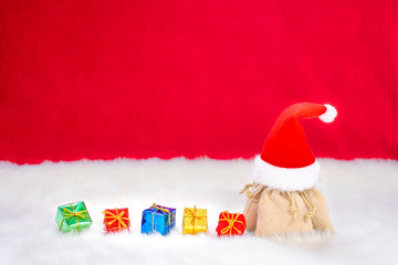 Weihnachtsgeschenke mit einer Weihnachtsmütze im Schnee vor einem Roten Hintergrund