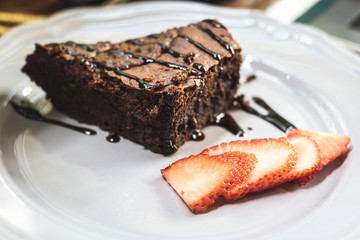 A piece of chocolate brownie with chocolate sauce and slice of strawberries.
