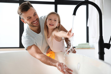 Father with his cute little daughter filling tub in bathroom