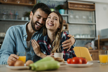 Young cheerful couple having fun during breakfast time in the kitchen. Man is in focus
