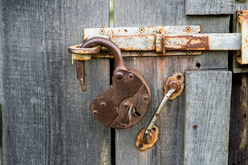 An antique open wrought iron lock with an inserted key hangs on the latch of an old wooden door. Background