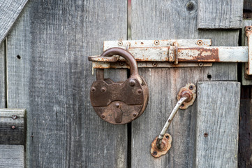 An old closed wrought-iron lock hangs on the bolt of an old wooden door. Background