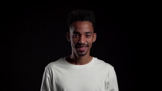Young african american man in white on black studio background showing yes sign by head. Positive footage, emotions, body language concept.