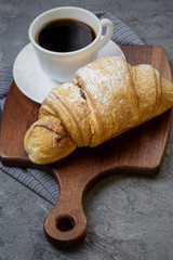 White Cup of coffee and large croissant on gray concrete table. French breakfast. Flat lay.