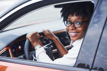 Young african american woman sits inside of new modern car