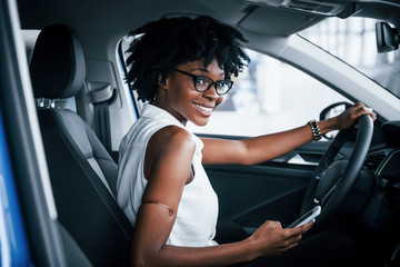 Using phone. Young african american woman sits inside of new modern car