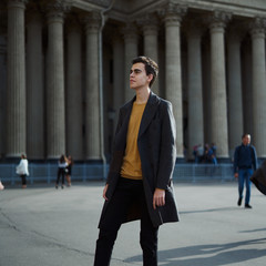 Handsome stylish fashionable man, brunette in elegant gray coat, stands on street in historical...