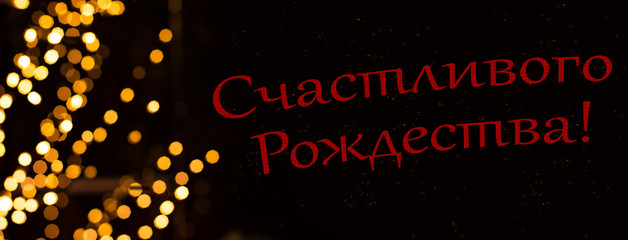 Russian language "Merry Christmas" text red letters on black background with golden bokeh garland illumination frame winter holidays happy time post card wallpaper picture concept 