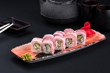 Japanese sushi roll with bacon and cream cheese with chopsticks and soy on black background. Sushi menu. Asian food and green tea teapot, copy space. Sashimi set.