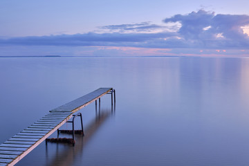 A jetty by the sea shining up on the side of the sun with clouds in background