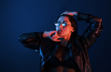 Hot brunette in sunglasses posing in the studio with neon lighting