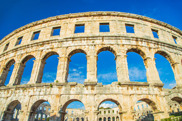 Obraz premium Ancient heritage in Pula, Istria, Croatia. Arches of monumental Roman arena. Detail of historic amphitheater, wide angle view of walls on blue sky background.