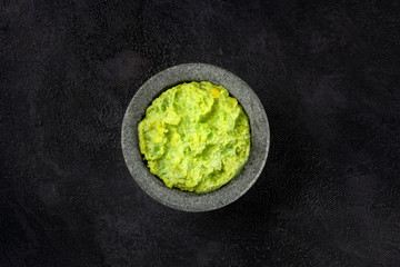 Guacamole in a molcajete, Mexican avocado dip in the traditional stone mortar, shot from the top on a black background - obrazy, fototapety, plakaty