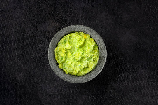 Guacamole in a molcajete, Mexican avocado dip in the traditional stone mortar, shot from the top on a black background