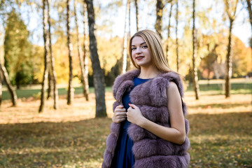Naklejka na ściany i meble Fashion woman. Smiling girl in fur coat posin in autumn park with trees and ivy