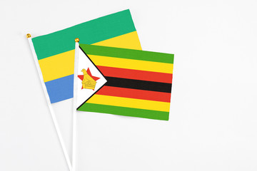 Zimbabwe and Gabon stick flags on white background. High quality fabric, miniature national flag. Peaceful global concept.White floor for copy space.