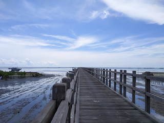 Fototapeta premium view of a long wooden bridge on the beach with a background of white clouds and beautiful blue sky