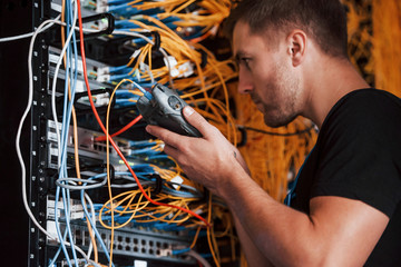 Young man in uniform works with internet equipment and wires in server room
