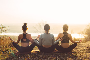 Three girls sitting in lotus position, rear view. Team Yoga Concept Outdoors