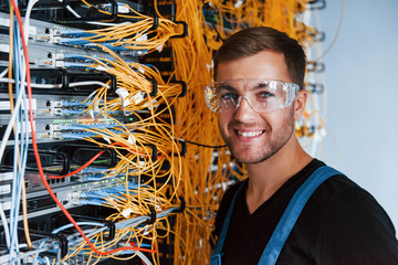 Young man in protective glasses works with internet equipment and wires in server room